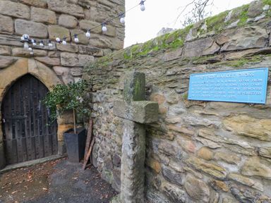 An old stone cross mounted on a stone wall with a blue information plaque and a wooden door nearby at Slaley Park Villa in Hexham