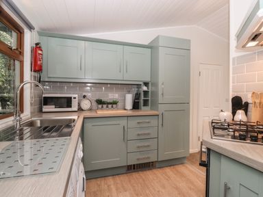 A kitchen with green cabinets a sink a microwave a stove and kitchen utensils at JacMar Lodge 14 Applethwaite Limefitt Park near Windermere