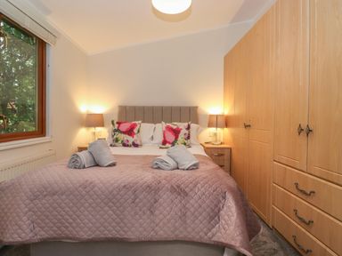 A bedroom with a double bed with pillows and rolled towels bedside tables with lamps and a large wooden wardrobe at JacMar Lodge 14 Applethwaite Limefitt Park near Windermere