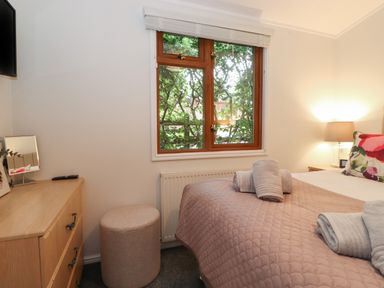 A bedroom with a bed covered by a quilted blanket with towels on it and a wooden dresser with a mirror and remote at JacMar Lodge 14 Applethwaite Limefitt Park near Windermere