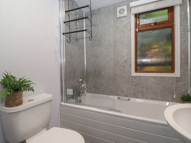 A bathroom with a bathtub shower combo a toilet with a plant and a window at JacMar Lodge 14 Applethwaite Limefitt Park near Windermere