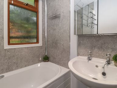 A bathroom with a bathtub, sink with two taps, a frosted window, a wall shelf, and a mirrored cabinet at JacMar Lodge 14 Applethwaite Limefitt Park near Windermere