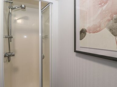 A shower with a glass door and a wall-mounted showerhead next to a wall with a framed abstract painting at JacMar Lodge 14 Applethwaite Limefitt Park near Windermere
