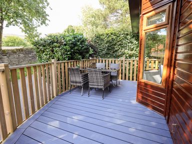 An outdoor deck with wicker chairs and a glass table next to a wooden cabin at JacMar Lodge 14 Applethwaite Limefitt Park near Windermere