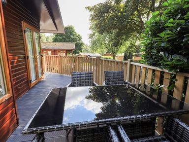 A balcony with a glass table and woven chairs overlooking trees at JacMar Lodge 14 Applethwaite Limefitt Park near Windermere