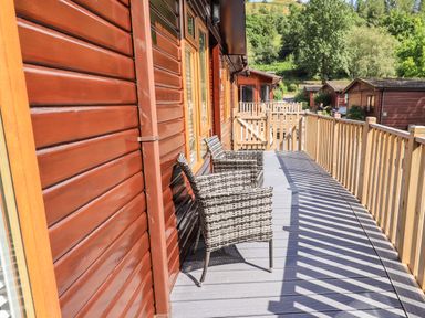 A wooden deck with two wicker chairs outside wooden cabins with a wooden railing at JacMar Lodge 14 Applethwaite Limefitt Park near Windermere