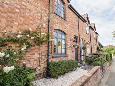 Brick exterior of a row of houses with gray window frames and doors with plants and flowers outside at Ross Cottage in Broadway