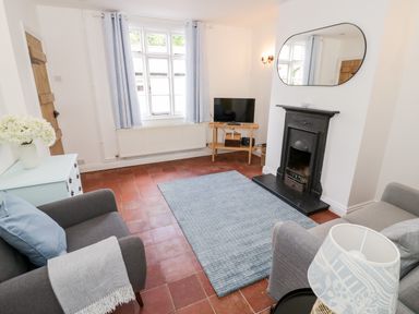 A living room with a fireplace a TV on a wooden stand two armchairs a blue rug and a window at Ross Cottage in Broadway