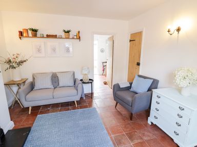 A living room with a sofa armchair shelf white dresser and flowers at Ross Cottage in Broadway