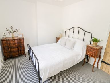 A bedroom with a metal bed frame white bedding two wooden bedside tables a wooden chest of drawers and striped carpet at Ross Cottage in Broadway