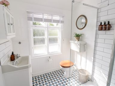 A bathroom with a toilet wooden seat sink with a brown bottle and a window with blinds at Ross Cottage in Broadway