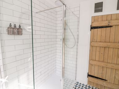 A shower area with white subway tiles and a glass door next to a wooden door with black hardware at Ross Cottage in Broadway