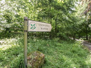 A signpost for Snowshill Manor surrounded by grass and trees at Ross Cottage in Broadway