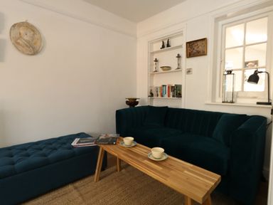 A living room with a blue sofa and ottoman a wooden coffee table with cups and books and a bookshelf at 26 High West in Weymouth