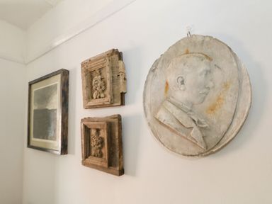 A white wall with three wooden framed decorations and a round relief sculpture of a man in profile at 26 High West in Weymouth