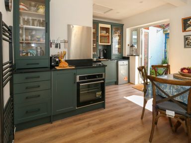 A kitchen with dark green cabinets a wooden dining table with chairs and an open door to a small outdoor area at 26 High West in Weymouth