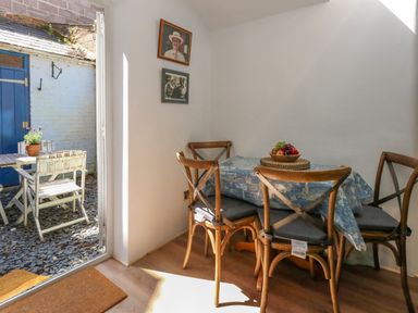 A dining area with four wooden chairs around a table covered with a blue tablecloth and a bowl of fruit at 26 High West in Weymouth