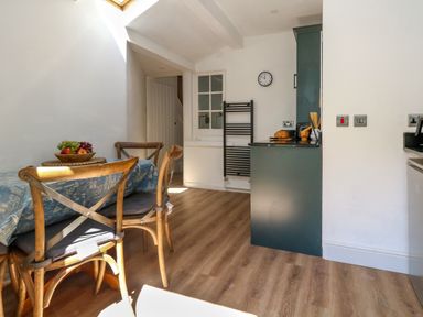 A kitchen dining area with wooden chairs around a table with a fruit bowl and a blue tablecloth at 26 High West in Weymouth