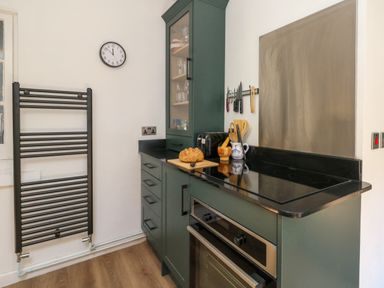 A kitchen with green cabinets a black countertop an oven a toaster a loaf of bread on a cutting board and a wall clock at 26 High West in Weymouth