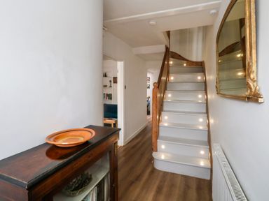 A hallway with wooden flooring a staircase with lights a wooden cabinet with an orange plate and a wall mirror at 26 High West in Weymouth