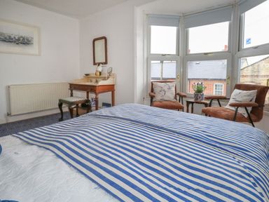 A bedroom with a bed blue striped bedding two chairs with cushions a small table and a dressing table at 26 High West in Weymouth