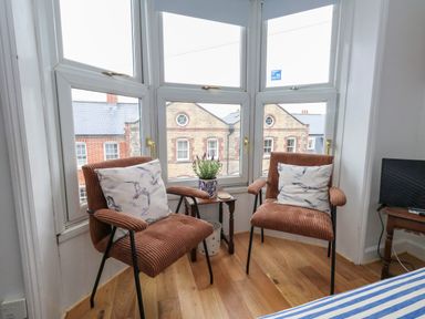 Two brown chairs with bird print cushions beside a small wooden table with a plant in front of bay windows in a room at 26 High West in Weymouth