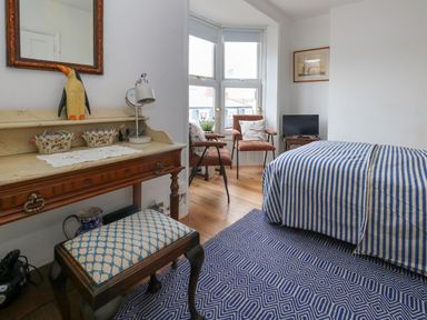 A bedroom with a striped bedspread a wooden desk with a lamp two chairs by a bay window and a small TV on a table at 26 High West Weymouth