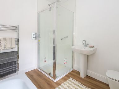 A bathroom with a glass shower cubicle a pedestal sink a towel rack with towels and a striped rug on a wooden floor at 26 High West in Weymouth