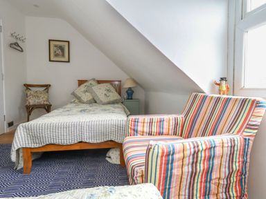 A bedroom with a bed pillows a striped armchair a wooden chair and a bedside table with lamp at 26 High West Weymouth