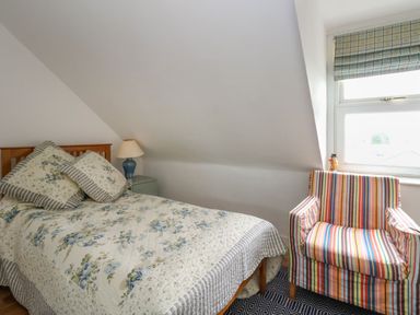 A bedroom with a bed a nightstand with a lamp a striped armchair and a window at 26 High West in Weymouth