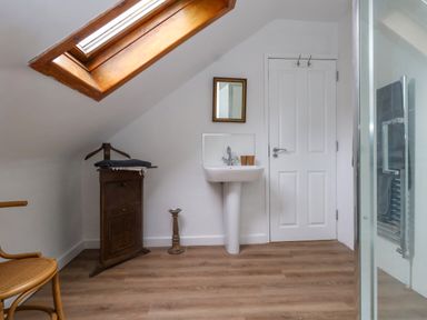 A bathroom with a wooden chair a wooden cabinet a white pedestal sink a mirror and a skylight window at 26 High West in Weymouth