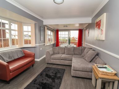 A living room with a brown leather sofa grey sectional sofa black rug and dining table with red curtains at Swiss Cottage in Wilsthorpe near Bridlington