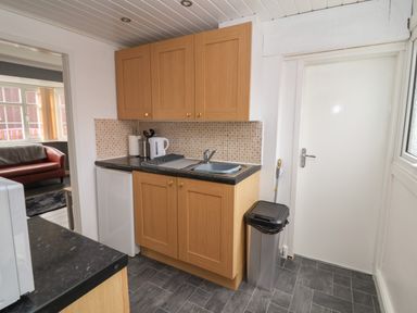 A kitchen with wooden cabinets a sink a kettle utensils and a trash bin at Swiss Cottage in Wilsthorpe near Bridlington