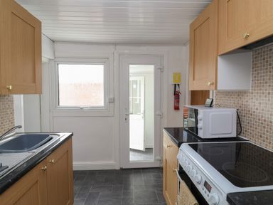 A kitchen with wooden cabinets a black countertop a microwave on the counter a white stove and oven a sink a window and a glass door at Swiss Cottage Wilsthorpe near Bridlington