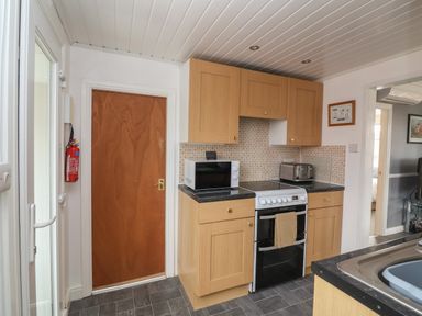 A kitchen with wooden cabinets a microwave stove toaster and a fire extinguisher at Swiss Cottage in Wilsthorpe near Bridlington
