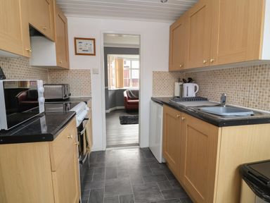 A kitchen with wooden cabinets black countertops a microwave toaster and a view into a living room at Swiss Cottage in Wilsthorpe near Bridlington