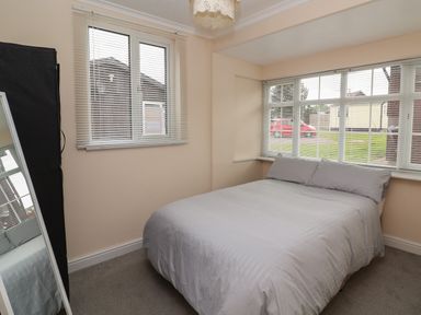 A bedroom with a double bed near corner windows and a standing mirror at Swiss Cottage in Wilsthorpe near Bridlington