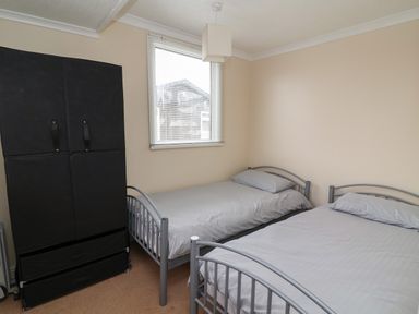 A bedroom with two single beds and a black wardrobe near a window at Swiss Cottage in Wilsthorpe near Bridlington