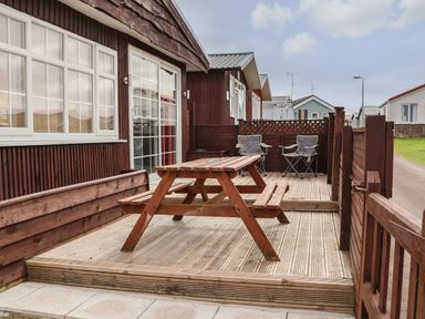 An outdoor wooden deck with a picnic table and two folding chairs at Swiss Cottage in Wilsthorpe near Bridlington