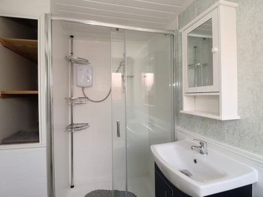 A bathroom with a glass-enclosed shower, a white sink with a faucet, a white wall-mounted cabinet with a mirror, and built-in shelves at Swiss Cottage in Wilsthorpe near Bridlington