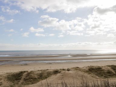 A sandy beach with grassy dunes and the sea under a cloudy sky at Swiss Cottage in Wilsthorpe near Bridlington