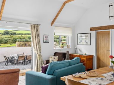 A living room with a blue sofa brown armchair wooden sideboard dining table with bread and outdoor seating area at The Farm Office in Bampton Devon