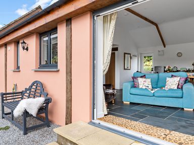 An open doorway showing a blue sofa with cushions inside and a black bench with a white throw outside at The Farm Office in Bampton Devon