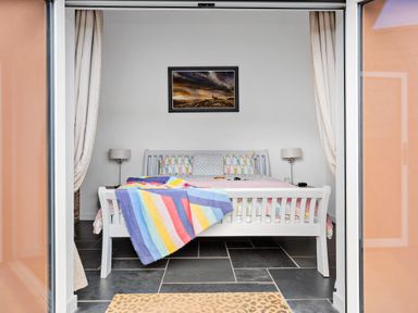 A bedroom with a white wooden bed a colorful striped blanket and a painting above the bed at The Farm Office in Bampton Devon