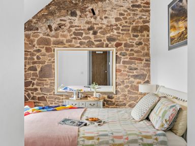 A bedroom with a bed covered in patterned bedding and a brick wall with a large mirror at The Farm Office in Bampton Devon