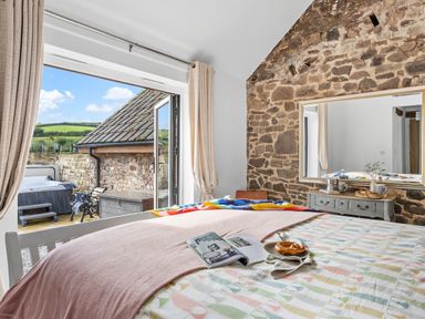A bedroom with a bed and an open door leading to an outdoor patio with a hot tub and a stone wall at The Farm Office in Bampton Devon
