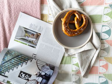 A pretzel on a plate with a napkin next to an open magazine on a patterned tablecloth at The Farm Office in Bampton Devon