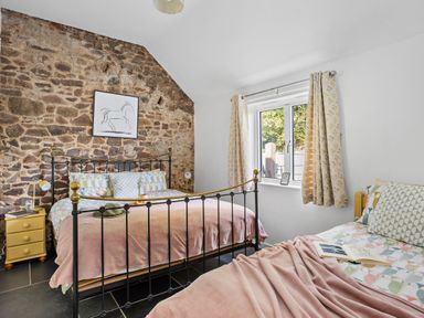 A bedroom with two beds a stone feature wall a window with curtains and bedside tables at The Farm Office in Bampton Devon