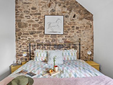 A bed with patterned bedding and pillows against a stone wall with a framed horse drawing above at The Farm Office in Bampton Devon
