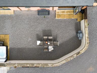 An outdoor gravel courtyard with a wooden table and four chairs a hot tub and a barbecue at The Farm Office in Bampton Devon